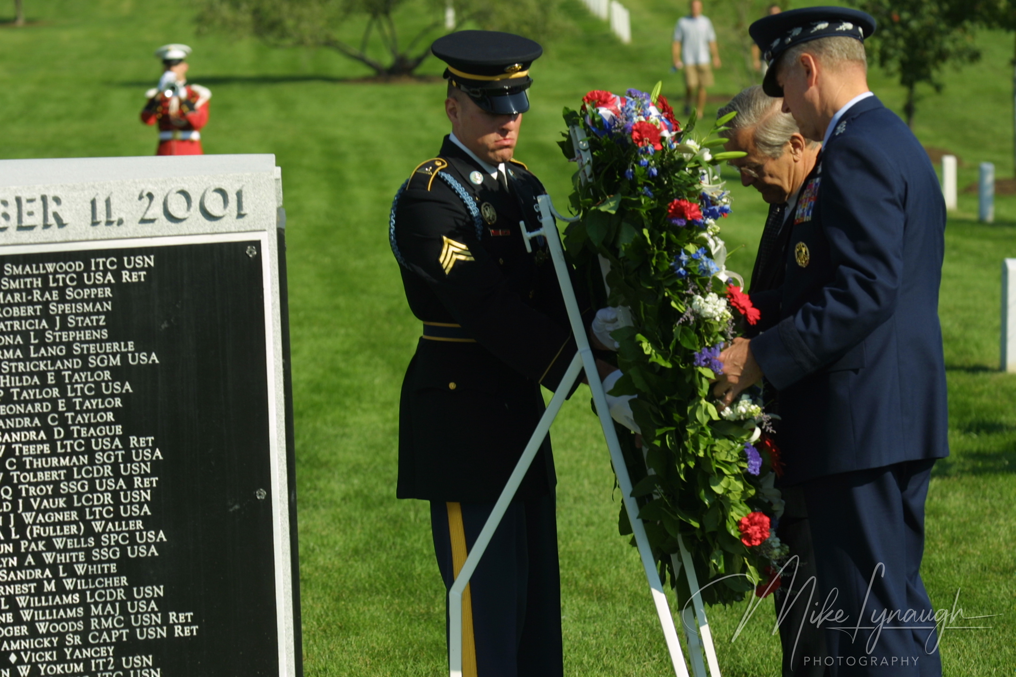 Secretary Donald Rumsfeld and General Richard Myers placing a floral wreath on a stand next to an Army honor guard guard and a granite headstone listing 9/11 victims