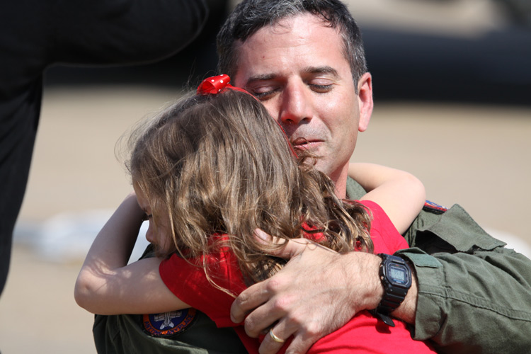 A military aviator embraces his daughter at a homecoming